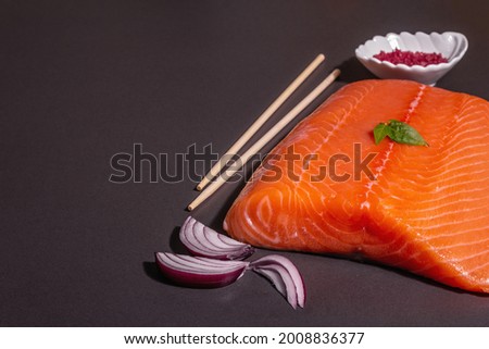 Fresh raw salmon or trout sea fish fillet on black stone background. Useful ingredient for healthy food, source of Omega 3. A modern hard light, dark shadow, culinary wallpaper, copy space