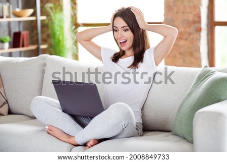Photo portrait brunette woman sitting on couch at home working on computer keeping head amazed