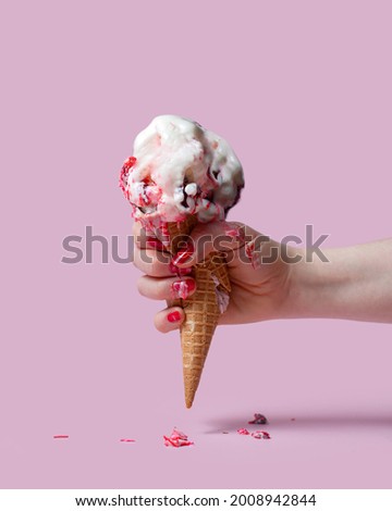 Female hand holds an ice cream cone on a pink background. The ice cream melted and ran down my fingers and hand. The hand squeezed and crushed the waffle glass. Anger, indignation.