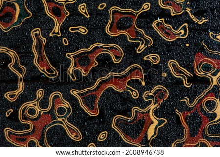 Red stain surrounded by golden lines on black background with droplet of water