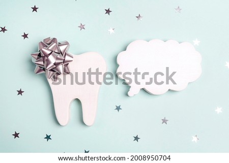 White tooth with a gift bow and empty speech bubble on a blue background with stars. Dental health care, dentist holiday.