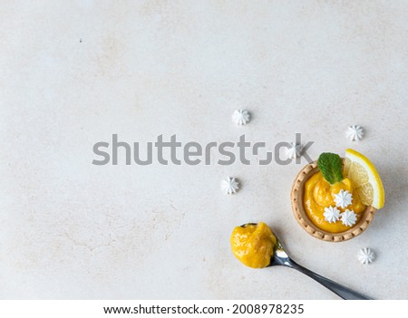 Shortbread mini tart with lemon curd, mint and lemon slices and mini meringue, light concrete background. Top view. Copy space.