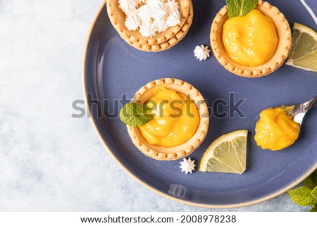 Lemon curd mini tarts decorated with mint and lemon slices on blue ceramic plate. Top view.