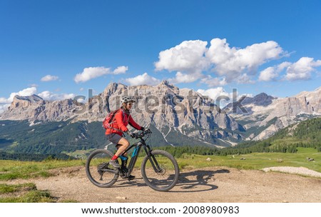 pretty beautiful senior woman riding her electric mountain bike on the Pralongia Plateau in the Alta Badia Dolomites with awesome Sasso die Santa Cruce summit in Backg, South Tirol and Trentino, Italy Royalty-Free Stock Photo #2008980983