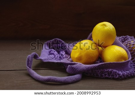 yellow lemons in purple string bag hang on wooden background