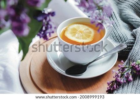 Spring composition flat lay with white cup of lemon tea, beautiful bouquet of lilacs, sweater. Concept of spring and comfort. Still life spring photography for card, poster, banner, wallpaper. 