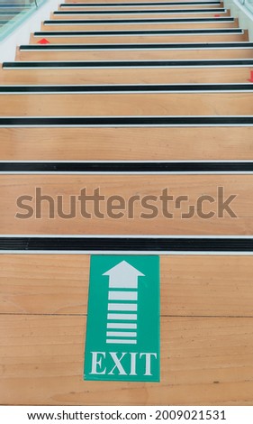 EXIT SIGN, down stairway design interior. a modern design with brown wooden staircase and clean glass hand rail combination. vertically captured on bright light inside an office for evacuation route 
