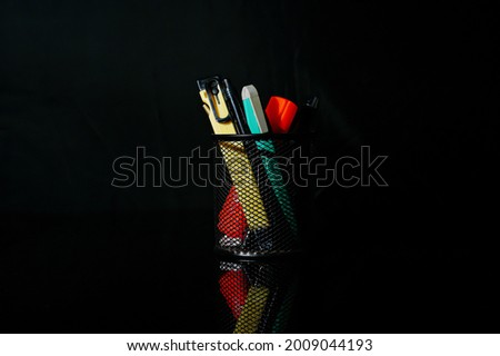 Isolated writing stationery supply in black metal web case on glass table and reflections