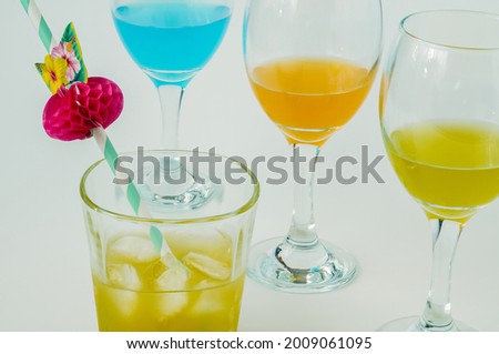 Glasses with yellow, blue and orange wine on a light background, alcohol in different colours, square glass with juice 