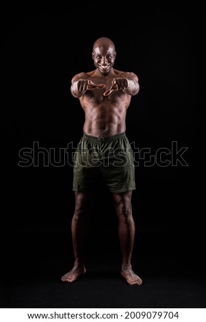 Black muscular man smiling standing and pointing at camera black background