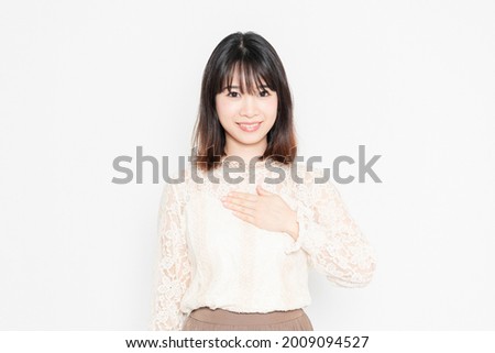 A young woman in a lace blouse standing in front of a white background and putting her hands on her chest