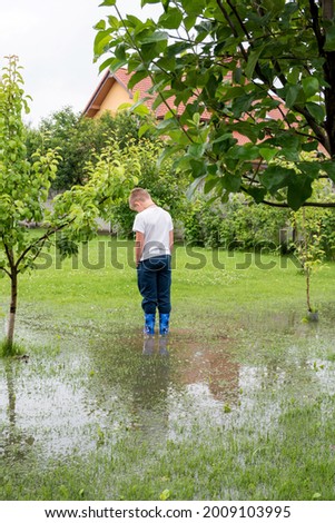 The garden is flooded. Consequences of downpour, flood. Rainy summer or spring.The child stands in the garden in the water, feet in rubber boots Royalty-Free Stock Photo #2009103995