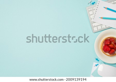Top view photo of keyboard mouse notebook blue pencils pins and plate with strawberry cupcake on isolated light blue background with copyspace