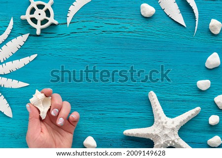Summer nautical abstract grungy background with white stones and exotic paper leaf silhouettes. Manicured hands with shell and starfish. Turquoise wood board. Flat lay, top view with copy-space.
