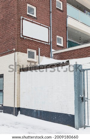 Back of a apartment building on a winter's day. Snow on the ground. Empty white banner on the wall. 