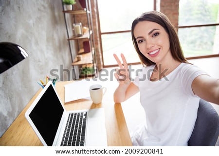 Photo portrait brunette woman sitting at table with laptop talking selfie showing v-sign gesture