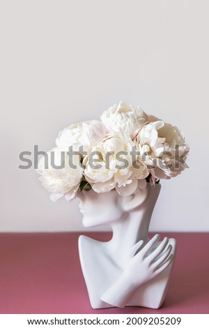 Fresh bunch of white peonies in vase in shape of womens face on dusty pink background. Trendy Ceramic Vase of human head, Handmade Modern Statue Art Flower Vase. Card Concept, copy space for text Royalty-Free Stock Photo #2009205209