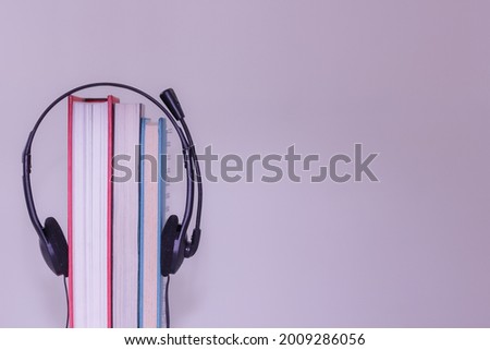 Headphone on the book. The subject is on the left hand side. with light purple color background. E Book and audio book concept. 