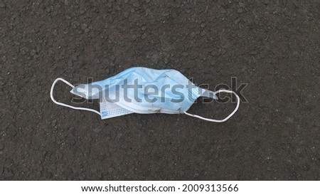 A medical mask is on the asphalt. After being used by the owner