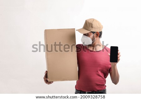 Delivery Man Wearing Medical Mask and Showing Smartphone screen with Box in Hands. Home Delivery. Order Online Technology.