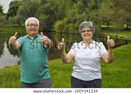 Cheerful energetic senior people enjoying sports exercise. Portrait of happy old couple standing in green park, looking at camera, smiling and giving thumbs up. Fitness and healthy lifestyle concept