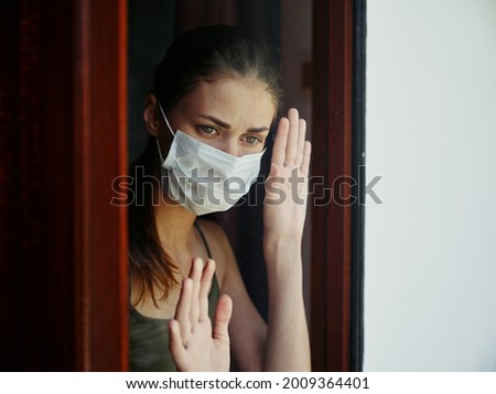 woman in medical mask sad look from the window prohibition