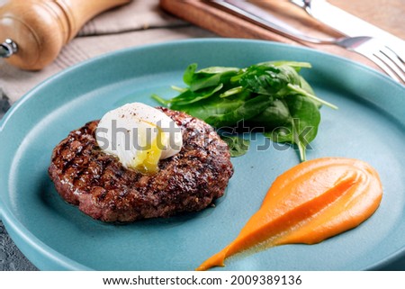 Minced beef steak with poached egg. Steak dish on a blue plate with spinach and pumpkin