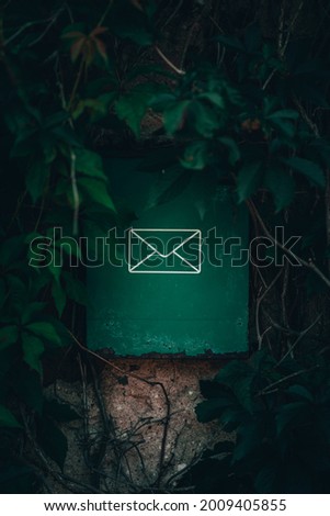 A mailbox hangs on the wall of an old house. There is a lot of green foliage around. Portrait mode