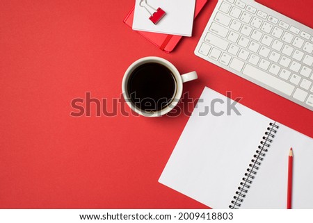 Top view photo of workplace white keyboard red binder clip pencil organizers and cup of coffee on isolated red background with copyspace