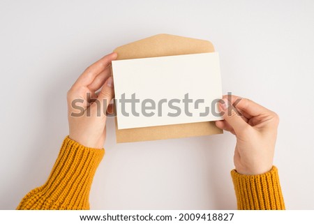 First person top view photo of female hands in yellow sweater holding open craft paper envelope and white card on isolated white background with blank space Royalty-Free Stock Photo #2009418827