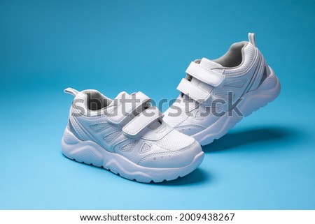 two white boys ' child shoes with velcro fasteners for the convenience of children's shoes, isolated on blue background.
