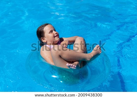 cheerful girl floating cross-legged and eyes closed on a blue inflatable circle in the hotel pool on a hot summer day.