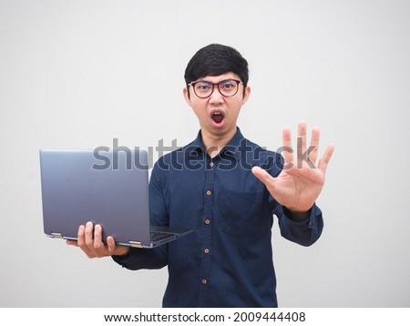 Asian man wearing glasses holding laptop and show hand up to stop with serious face white background