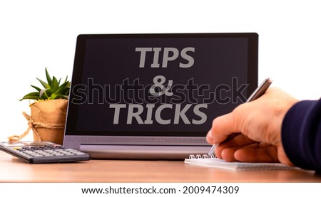 Tips and tricks symbol. Tablet with words 'Tips and tricks'. Businessman hand with pen, house plant. Beautiful white background. Business, tips and tricks concept, copy space.
