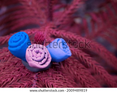 hand made three clay art blueish flower kept on thorn leaves surface at natural blur background.