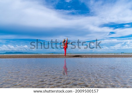 Asian young healthy woman posing practice bird of paradise yoga on beach with blue cloud sky and sea background in healthy exercise lifestyle concept