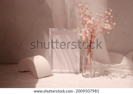 Retro interior still life with geometric shape, picture frame with paper sheet, gypsophila flowers in the glass bottle. Minimalist beige design mock up. Sunlight and shadows pattern.