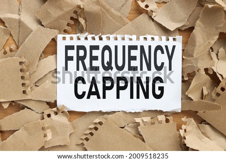 FREQUENCY CAPPING, text on white paper on torn kraft paper background