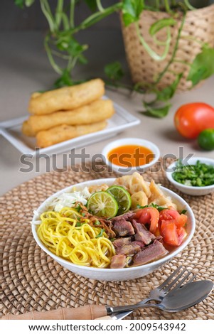 Soto Mie Bogor, Indonesian traditional beef noodle soup from West Java with noodles, beef, spring roll, cabbage, and tomato. Served with chili sauce and lime. Royalty-Free Stock Photo #2009543942
