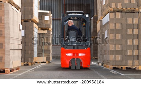 Expreinced forklift driver is driving his forklift backwards trough piled pallets with  cardboardboxes stack on it.  Royalty-Free Stock Photo #200956184