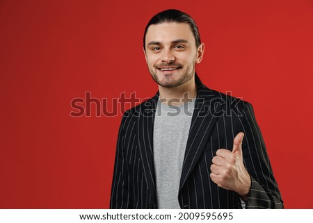 Young smiling businessman latin man 20s with long hair ponytail wear black striped jacket grey shirt show thumb up like gesture isolated on red background studio portrait. Concept of people lifestyle
