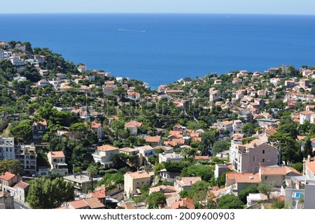 View of residential hills with green trees and light pink houses on the French Riviera, with the Mediterranean sea in the background, on a sunny day with clear sky. Royalty-Free Stock Photo #2009600903