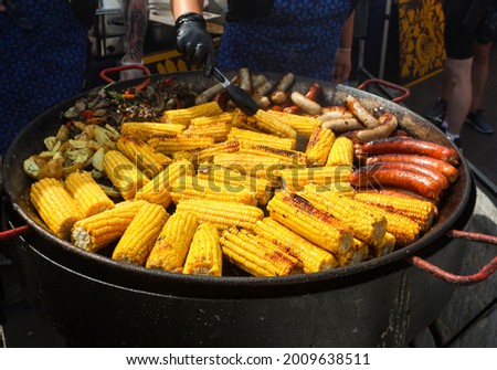 Corn fried on the fire. 
Grilled sausage with the addition of herbs and vegetables on the grill plate, outdoors. Grilling food, bbq, barbecue