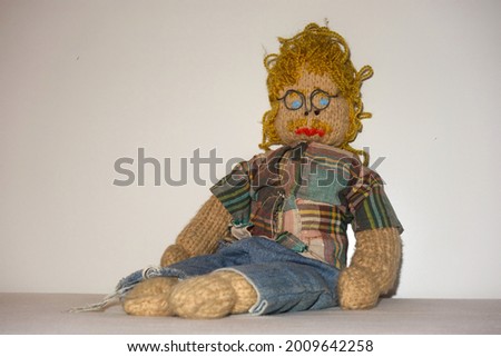 Stereotype : engineer with a plaid shirt, horn-rimmed glasses, blue eyes, curly blond hair and a mustache sits against a neutral white background . Male knitted doll . Cute guy in nerd look .