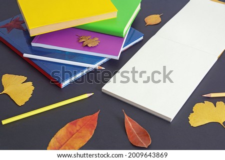 School concept. Stack of books, colorful colored pencils and open sketchbook on dark paper background. Autumn leaves. Free space for text or picture