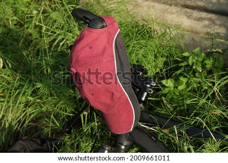 red black cap made of fabric hangs on the handlebars of a sports bike in the green grass and vegetation on the street