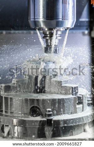 Vertical photo of industrial wet milling process in 5-axis cnc machine with coolant flow under pressure and freezed splashes.