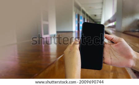 Smart phone hold in hands with blur brown porch and bench of building at school in background, concept of using technology device to contact parents  