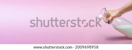 A jug of milk on a pink background in a woman's hand. Milk in a glass bottle. Space for text, large banner.