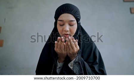 Young muslim woman wears traditional black clothes sitting on mat, makes traditional prayer to God, keeps hands in praying gesture  at home